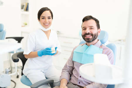 Confident good looking female orthodontist holding smile design model while sitting by patientの写真素材