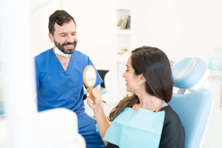 Smiling male orthodontist looking at woman holding mirror after orthodontic treatmentの写真素材