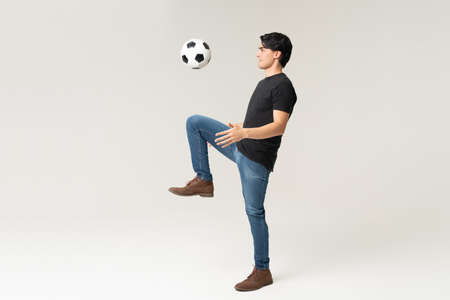 Full length of handsome young man in casuals playing with soccer ball in studio