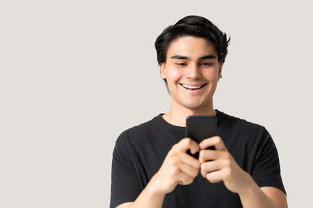 Handsome Hispanic man smiling while texting on smartphone against gray backgroundの写真素材