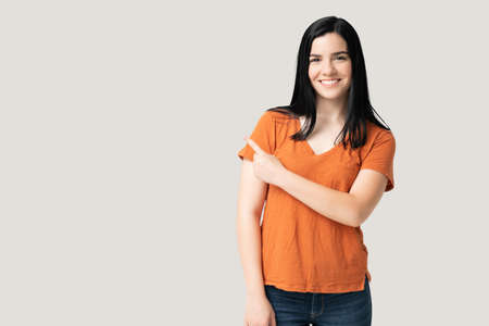 Pretty smiling young woman isolated on gray background pointing with finger at copy space