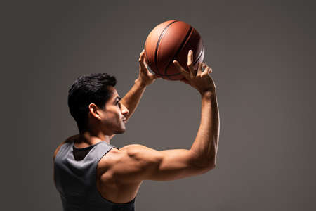 Hispanic young basketball player throwing ball while practicing in studioの写真素材