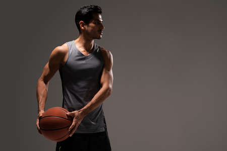 Handsome Hispanic young male athlete with basketball against gray backgroundの写真素材