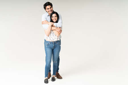 Smiling boyfriend hugging good looking girlfriend while standing against white background