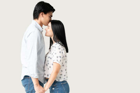 Handsome young man holding hands of girlfriend kissing her foreheadの写真素材