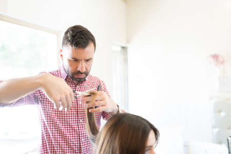 Male hairdresser cutting hair of female customer at beauty salonの写真素材