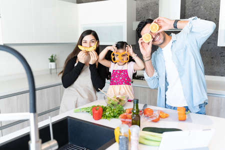 Playful family with fruits and vegetables preparing food at homeの写真素材