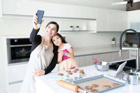 Smiling Latin family taking selfie while preparing cookies at home
