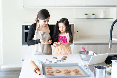 Smiling mother and cute daughter learning to prepare cookies in kitchen at homeの写真素材