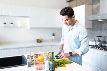 Good looking young man chopping vegetables at kitchen islandの写真素材