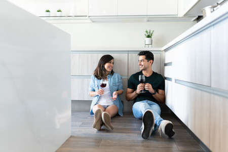 Latin young couple talking while drinking wine in kitchenの写真素材