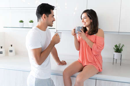 Smiling young couple looking at each other while drinking coffee in kitchen at home