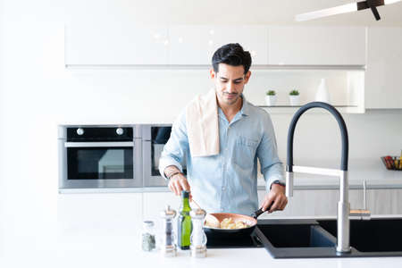 Hispanic young man cooking pasta in pan at kitchen island