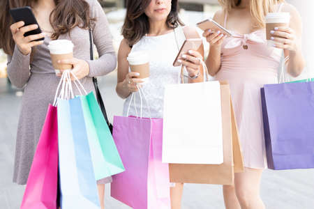 Midsection of women with shopping bags and disposable coffee cups using smartphonesの写真素材