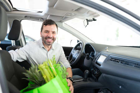 Smiling good looking Latin man sitting with grocery bag in carの写真素材