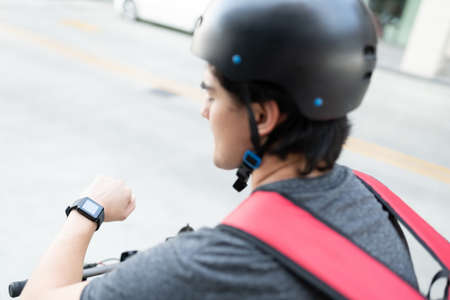 Delivery man checking time on smartwatch while cycling in cityの写真素材