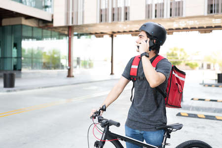 Young delivery man searching address while talking on mobile phone on streetの写真素材