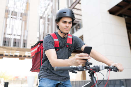 Handsome courier delivery man using map on smartphone while riding bicycle
