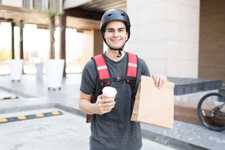 Confident Hispanic delivery man holding parcel and disposable coffee cupの写真素材