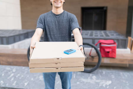 Midsection of delivery man with credit card reader on stack of pizza boxesの写真素材