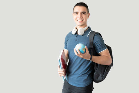 Hispanic university exchange student holding a small globe and carrying a backpack ready for school,...