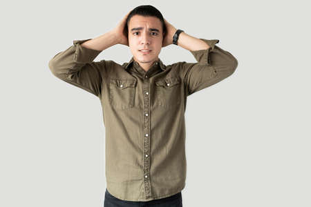 Handsome guy in casual clothing holding hands on his head and looking stressed while making eye...
