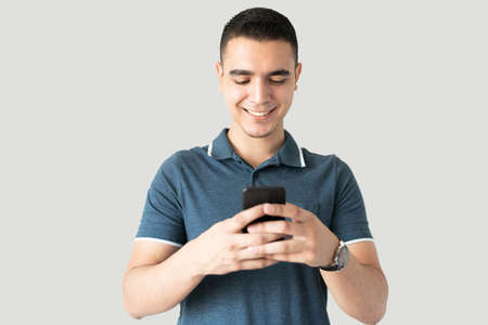 Good looking young man using his smartphone to check on social media in a studio and smiling