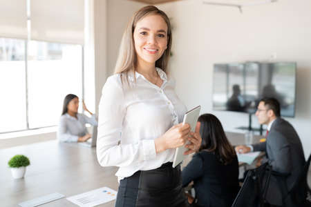 Portrait of a confident young caucasian businesswoman with a digital tablet standing in meeting room