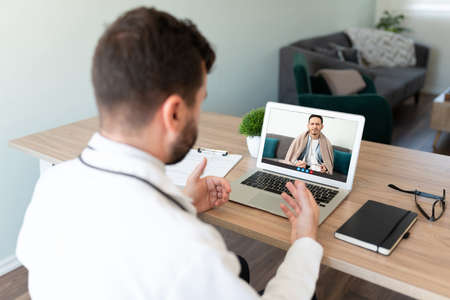Rear view of a male doctor giving medical advice to a sick patient online during a video callの写真素材