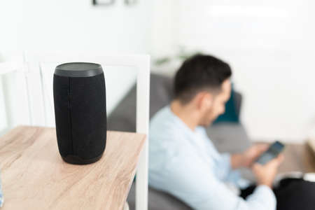 Young man setting up his smart speaker in his home. Focus on speaker in the foreground