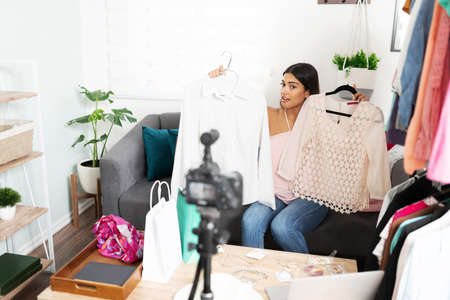 Cute Latin influencer and blogger asking her followers which piece of clothing they like more during a live video from homeの写真素材