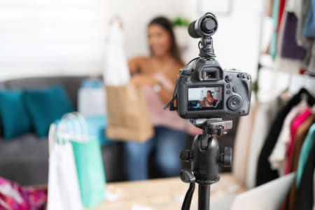 Closeup of a dslr camera recording a fashion video blogger while she shows some clothes to her...
