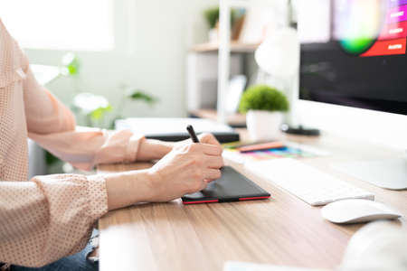 Profile view of the hands of a woman working as a designer and using a graphic tablet in her office