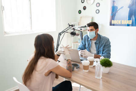 Blogger and podcast host interviewing a guest artist while wearing masks and gloves during an online...