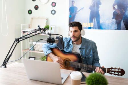 Handsome Latin musician playing the guitar and recording a song in a studio during a live podcastの写真素材