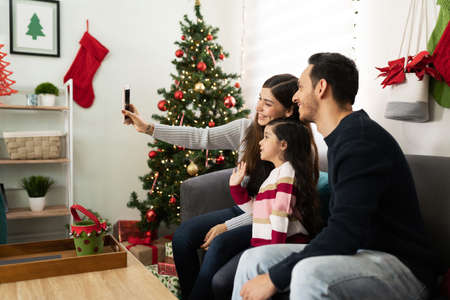 Latin family enjoying Christmas at home and doing a video call on a smartphone with some relatives to keep a safe distanceの写真素材