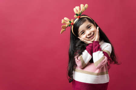 Beautiful little girl looking endearing and sweet on Christmas Holidays against a red background