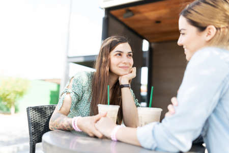 Romantic latin young woman making eye contact with a caucasian young woman while holding hands...
