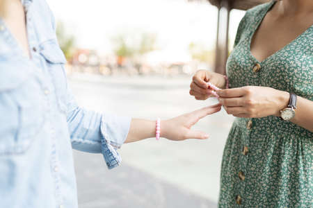 Close up of a young woman giving her woman friend a matching friendship pink braceletの写真素材