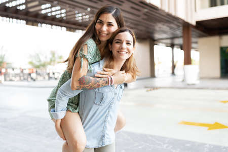 Caucasian lesbian young woman looking happy and giving a piggyback to her hispanic gay girlfriendの写真素材