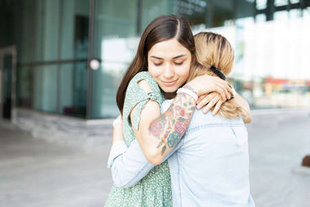 Latin young gay woman looking peaceful and happy while embracing her blond lesbian girlfiend outside...