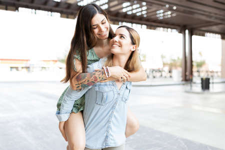 Cute lesbian couple having fun and making eye contact while one is on the back of her girlfriendの写真素材