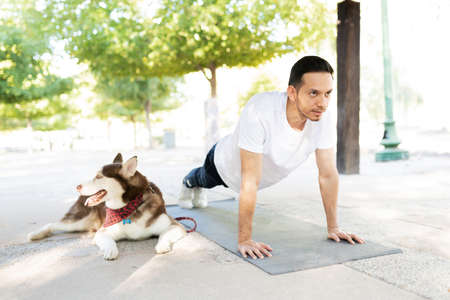 Good-looking latin man in his 30s working out and doing a plank next to his cute dog at the park