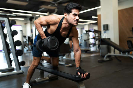 Strong hispanic young man doing a weight lifting workout in a bench at the fitness clubの写真素材