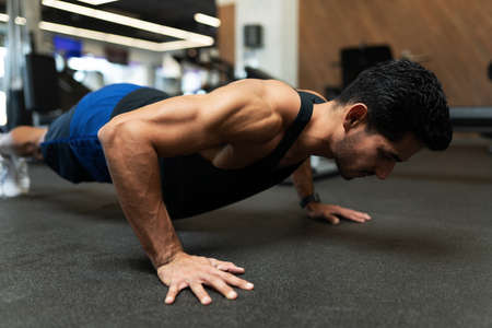 Side view of a muscular latin young man doing a workout with push ups in the gym floor