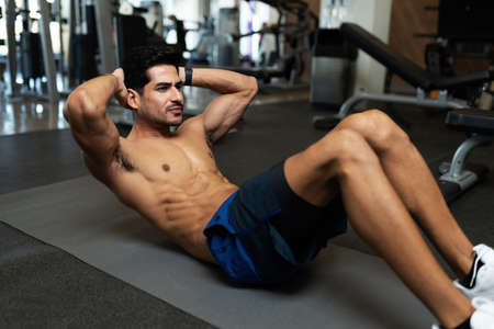 Muscular young man doing sit up exercises for his abdomen on a mat at the gym floor