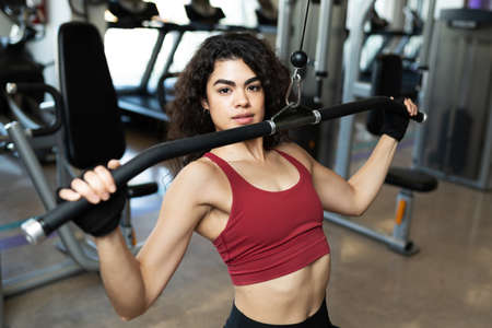 Portrait of a fit latin woman doing exercises with a cable machine at the gym