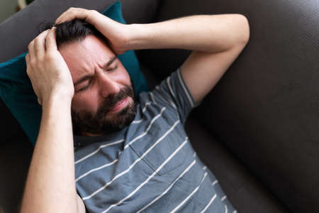 Close up of an adult man lying on the sofa with his hands in the head and an expression of frustration and anguishの写真素材