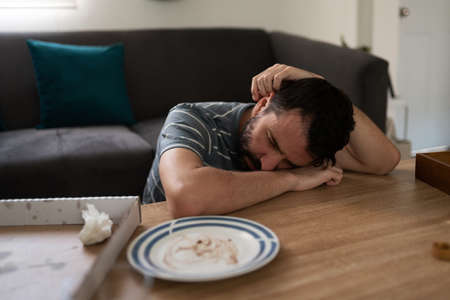 Man in his 30s looking depressed with his eyes closed and resting his head on the coffee table