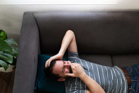 Latin man seen from above lying on the sofa and crying, looking sad and depressed in his home